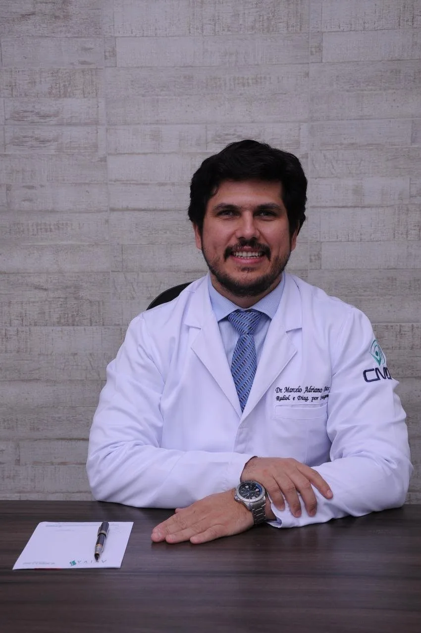 Dr. Marcelo Adriano Dias sentado à mesa do consultório